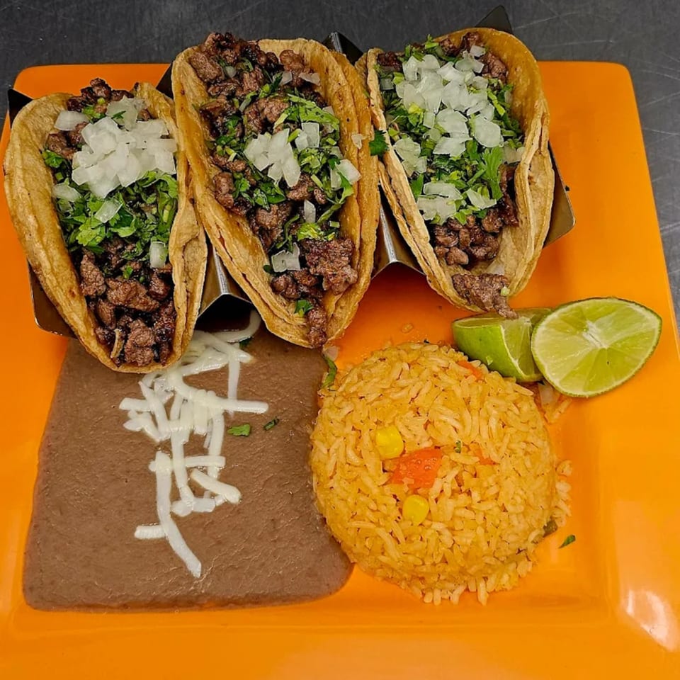 Three Mi Tierra Mexican Grill steak tacos with cilantro and onions, served with rice, beans, and lime.