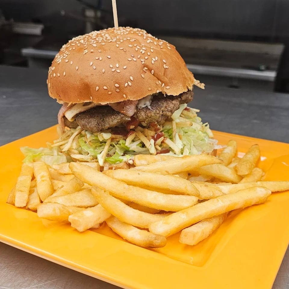 A Mi Tierra Mexican Grill burger with shredded lettuce, fries, and a sesame seed bun on a yellow plate.