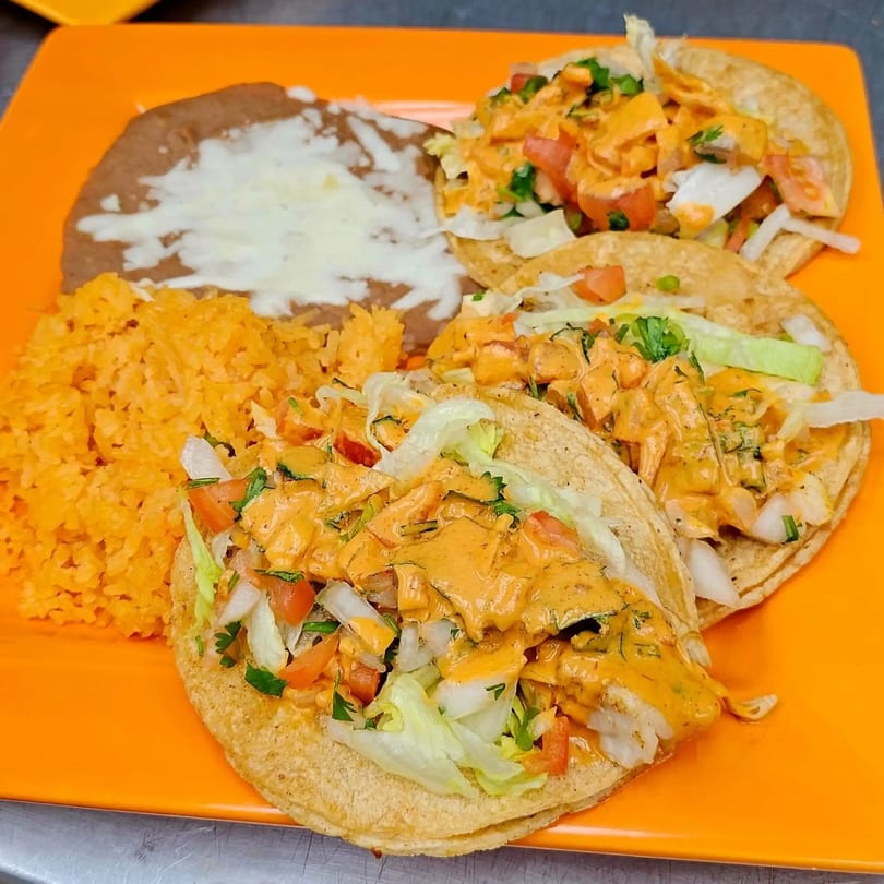 Three Mi Tierra Mexican Grill tacos with rice and refried beans on an orange plate.