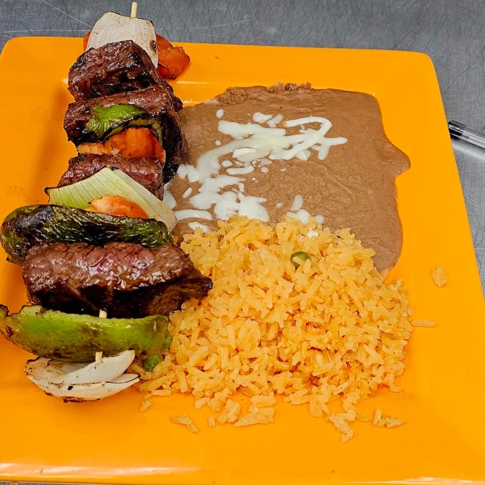 Mi Tierra Mexican Grill's beef and vegetable skewer with rice and refried beans on an orange plate.