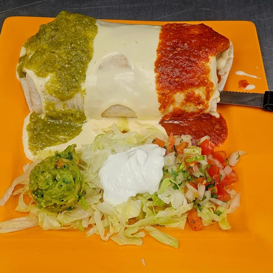 Mi Tierra's burrito covered in green and red sauce, with guacamole, sour cream, and pico de gallo.