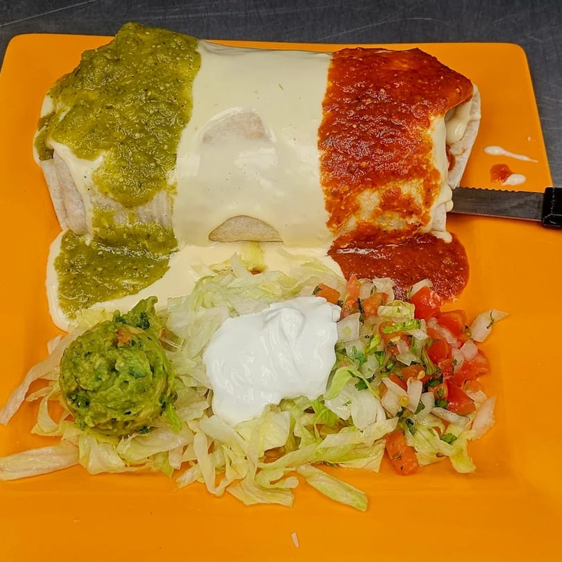 Mi Tierra's burrito covered in green and red sauce, with guacamole, sour cream, and pico de gallo.