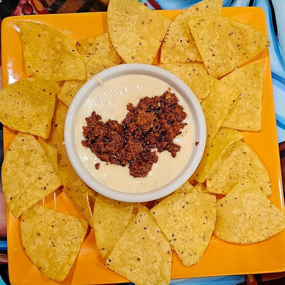 Mi Tierra's queso dip with chorizo, surrounded by tortilla chips on an orange plate.