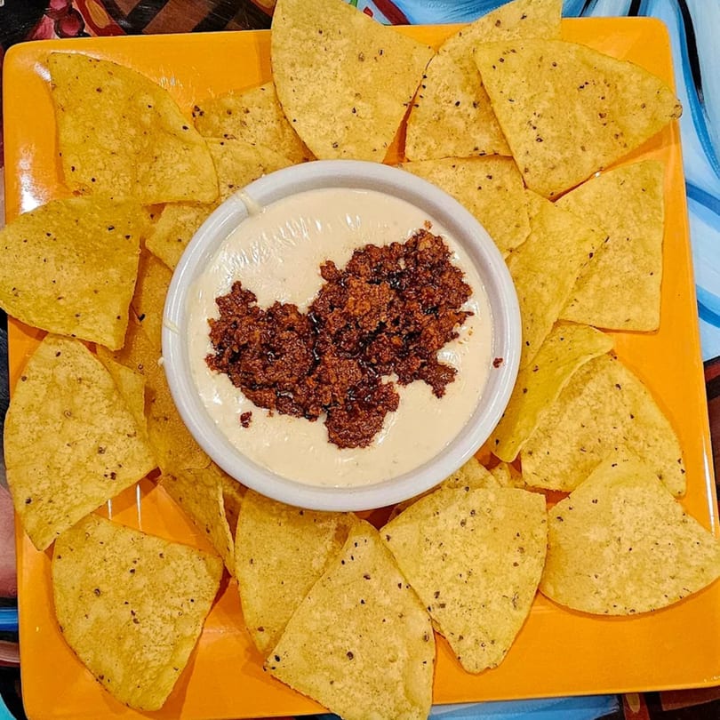 Mi Tierra's queso dip with chorizo, surrounded by tortilla chips on an orange plate.