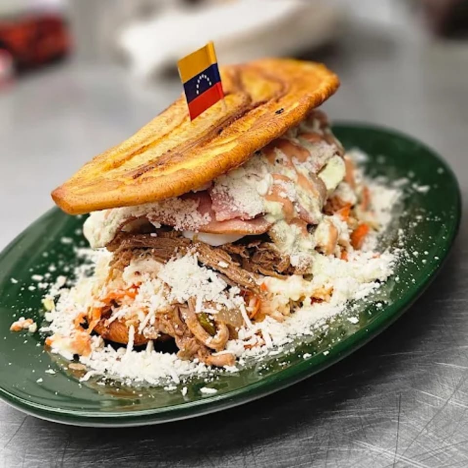 A Venezuelan patacon with shredded beef, ham, cheese, and sauce, topped with a Venezuelan flag.