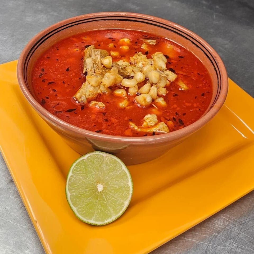 A bowl of Mi Tierra's red pozole with hominy and pork, garnished with a lime slice.