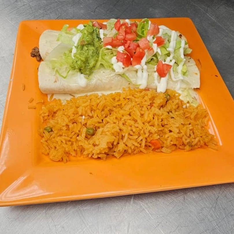 A Mi Tierra Mexican Grill burrito topped with lettuce, tomatoes, sour cream, and guacamole, served with rice.
